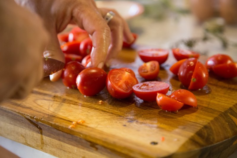 Tomaten werden mit einem Tomatenmesser auf einem Holzbrett halbiert.