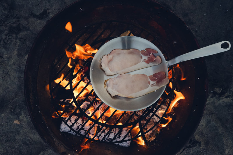Fleisch wird in einer handgeschmiedeten Pfanne über dem offenen Feuer gebraten