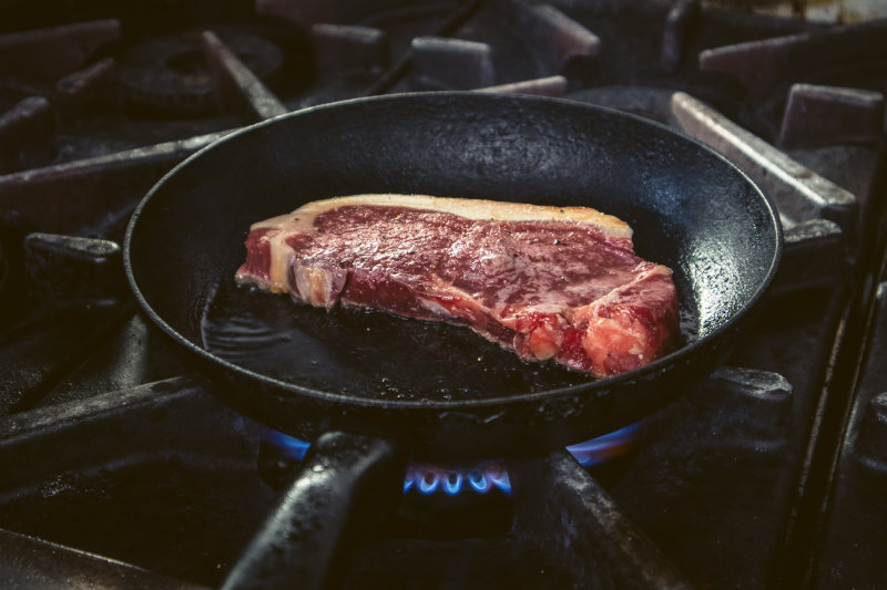 Steak braten in handgeschmiedeter Pfanne auf einem Gasherd gebraten