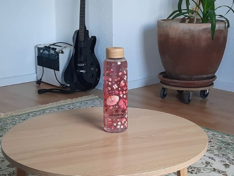 Eine mit Blumen bedruckte Waterdrop-Flasche auf einem runden Holztisch